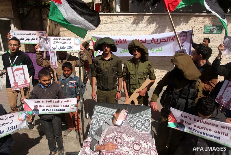 Palestinians enact a scene of Israeli soldiers and a boy lying in a bed in reference to Khaled al-Sheikh, a 14-years-old Palestinian boy jailed in an Israeli prison, during a rally calling for his release in Gaza City Fe...