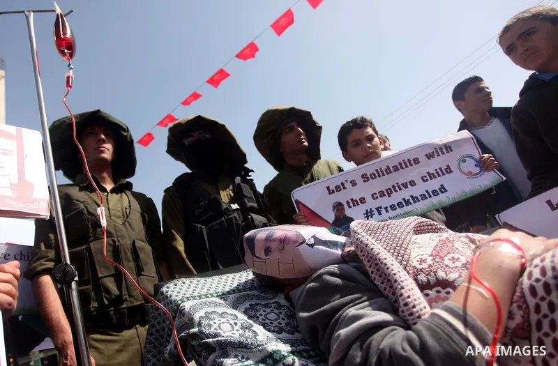 Palestinians enact a scene of Israeli soldiers and a boy lying in a bed in reference to Khaled al-Sheikh, a 14-years-old Palestinian boy jailed in an Israeli prison, during a rally calling for his release in Gaza City Fe...