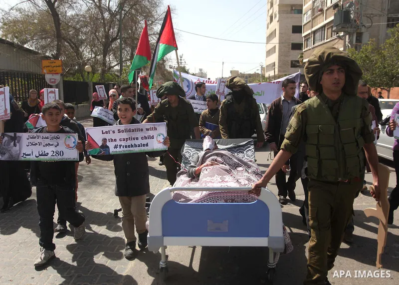 Palestinians enact a scene of Israeli soldiers pushes a boy lying in a bed in reference to Khaled al-Sheikh, a 14-years-old Palestinian boy jailed in an Israeli prison, during a rally calling for his release in Gaza City...