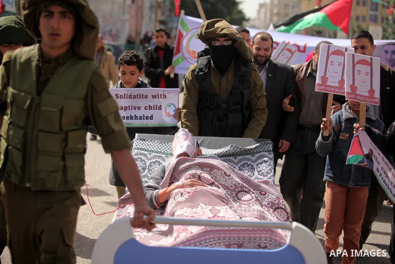 Palestinians enact a scene of Israeli soldiers pushes a boy lying in a bed in reference to Khaled al-Sheikh, a 14-years-old Palestinian boy jailed in an Israeli prison, during a rally calling for his release in Gaza City...