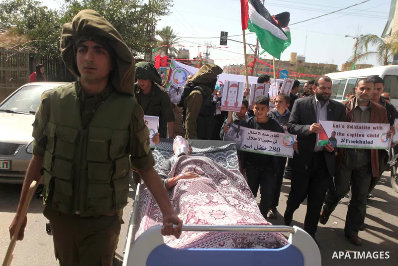 Palestinians enact a scene of Israeli soldiers pushes a boy lying in a bed in reference to Khaled al-Sheikh, a 14-years-old Palestinian boy jailed in an Israeli prison, during a rally calling for his release in Gaza City...