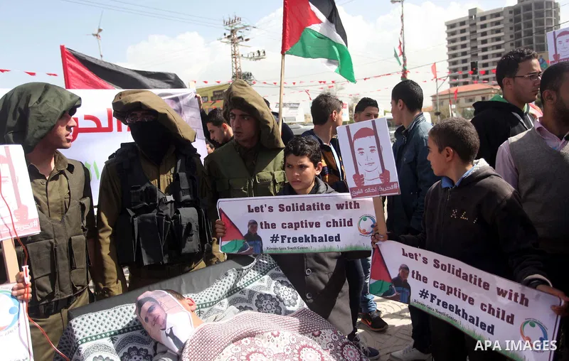 Palestinians enact a scene of Israeli soldiers and a boy lying in a bed in reference to Khaled al-Sheikh, a 14-years-old Palestinian boy jailed in an Israeli prison, during a rally calling for his release in Gaza City Fe...