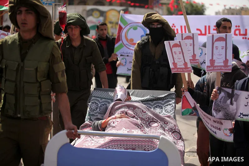 Palestinians enact a scene of Israeli soldiers pushes a boy lying in a bed in reference to Khaled al-Sheikh, a 14-years-old Palestinian boy jailed in an Israeli prison, during a rally calling for his release in Gaza City...
