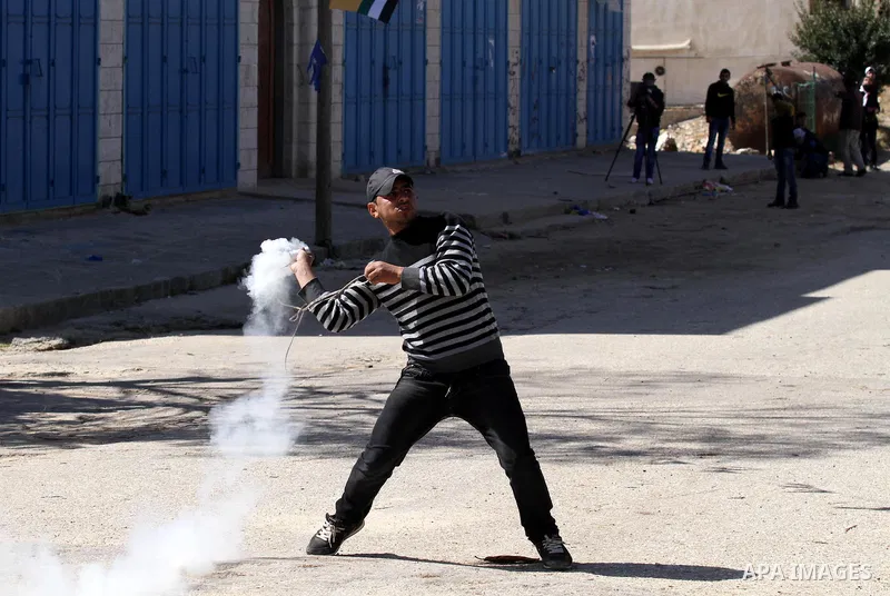 A Palestinian protester throws back a tear gas canister fired by Israeli security forces during clashes in the West Bank village of Azzun, following a protest against the closure of the main road in the village, near the...