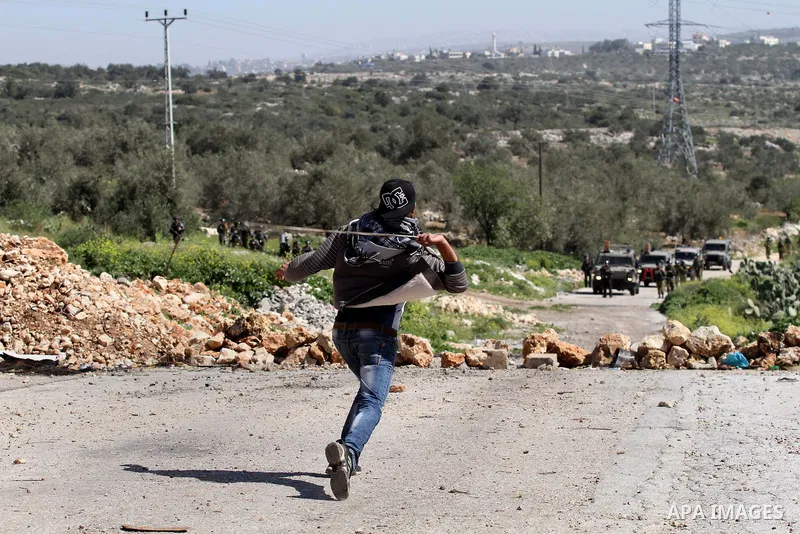 A Palestinian protester uses a sling shot to throw stones towards Israeli security forces during clashes in the West Bank village of Azzun, following a protest against the closure of the main road in the village, near th...
