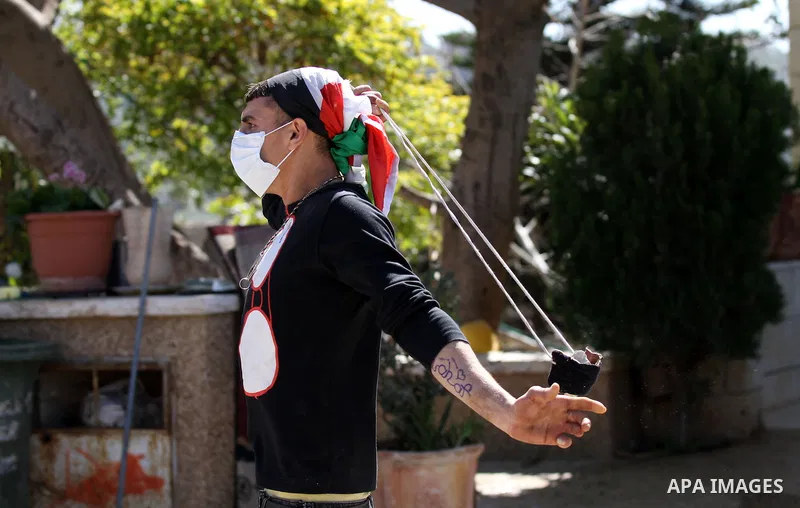 A Palestinian protester uses a sling shot to throw stones towards Israeli security forces during clashes in the West Bank village of Azzun, following a protest against the closure of the main road in the village, near th...