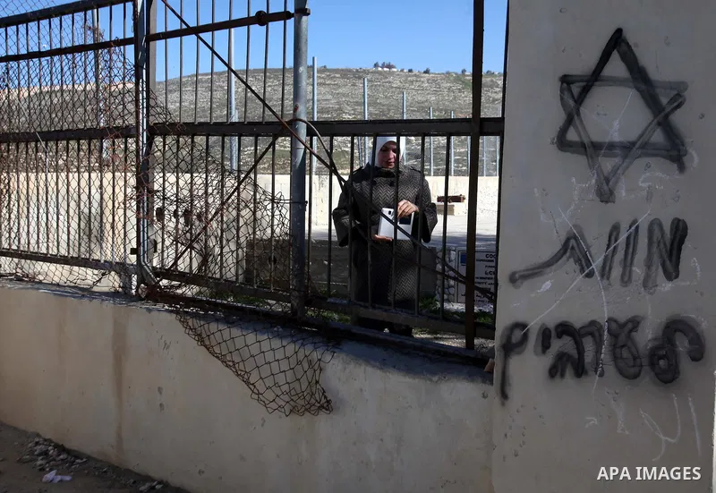 A Palestinian woman walks near a graffiti reads "death to Arab" including a Star of David, sprayed on the wall of a school in the Village of Urif by Israeli settlers, near the West Bank city of Nablus, February 26, 2015....