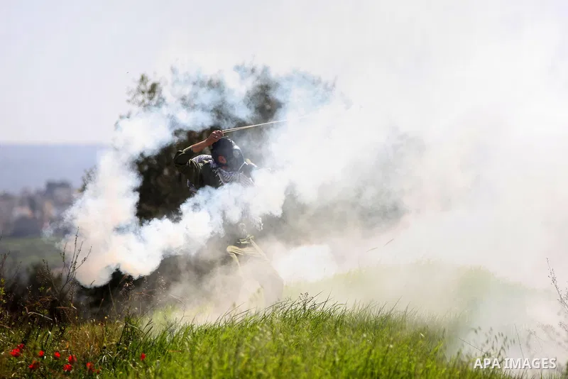 A Palestinian protester uses a sling shot to hurls back a tear gas canister fired by Israeli security forces during clashes following a demonstration against Jewish settlements in the West Bank village of Bilin, west of...