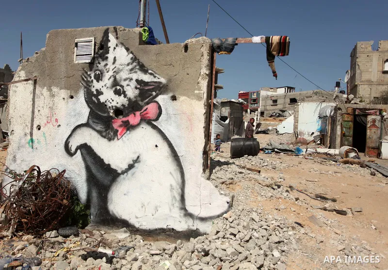 Palestinians walk near a mural of a kitten, said to have been painted by British street artist Banksy, on the remains of a house that was destroyed during the 50-day war between Israel and Hamas militants in the summer o...