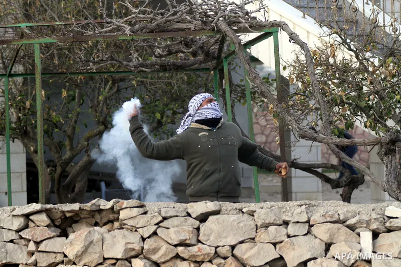 A Palestinian protester throws back a tear gas fired by Israeli security forces during clashes following a protest against what Palestinians say is land confiscation for Jewish settlements, in the West Bank village of Si...