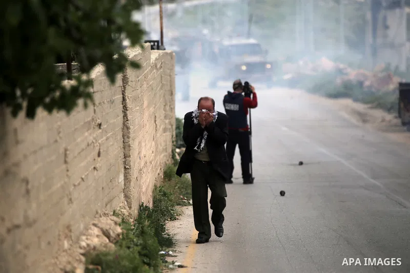 A Palestinian man covers his face from tear gas fired by Israeli security forces during clashes with Palestinian protesters following a protest marking the Palestinian Land Day in the West Bank village of Nabi Saleh near...