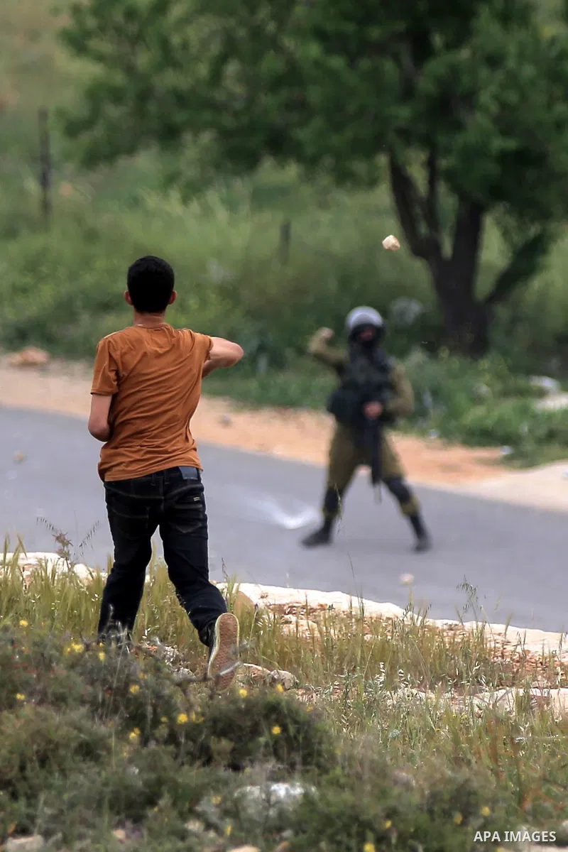 A Palestinian protester throws stones towards a member of Israeli security forces during clashes following a protest marking the Palestinian Land Day in the West Bank village of Nabi Saleh near Ramallah, March 28, 2015....