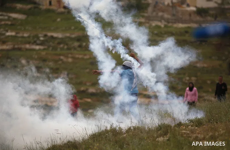 A Palestinian protester uses a sling shot to throw back a tear gas canister fired by Israeli security forces during clashes following a protest marking the Palestinian Land Day in the West Bank village of Nabi Saleh near...