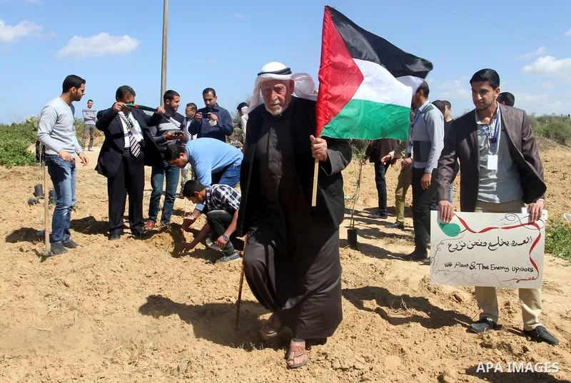A Palestinian man holds his national flag as Palestinians plant olive trees to mark Land Day during a symbolic ceremony held in the village of Abassan, east of Khan Yunis near the border fence between Israel and the sout...