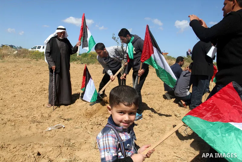 Palestinians hold their national flags as they plant olive trees to mark Land Day during a symbolic ceremony held in the village of Abassan, east of Khan Yunis near the border fence between Israel and the southern Gaza S...