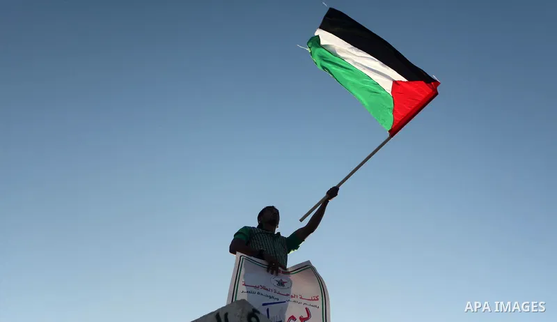 A Palestinian man holds a banner and waves a Palestinian flag during a gathering in solidarity with the Palestinians living in Syria's Yarmouk camp, which is besieged by government forces and has been largely overrun by...