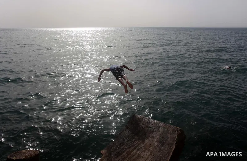 A Palestinian youth jumps into the Mediterranean Sea as he enjoys a warm day at the seaport in Gaza City on April 8, 2015. Photo by Ashraf Amra