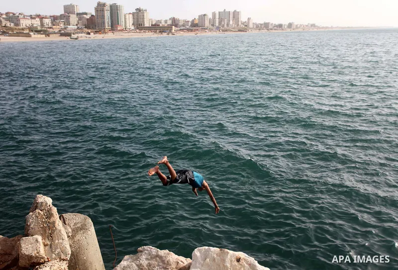 A Palestinian youth jumps into the Mediterranean Sea as he enjoys a warm day at the seaport in Gaza City on April 8, 2015. Photo by Ashraf Amra