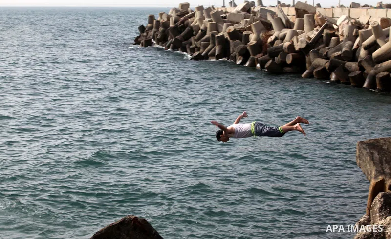A Palestinian youth jumps into the Mediterranean Sea as he enjoys a warm day at the seaport in Gaza City on April 8, 2015. Photo by Ashraf Amra