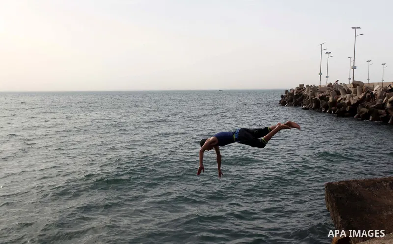A Palestinian youth jumps into the Mediterranean Sea as he enjoys a warm day at the seaport in Gaza City on April 8, 2015. Photo by Ashraf Amra