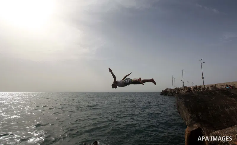 A Palestinian youth jumps into the Mediterranean Sea as he enjoys a warm day at the seaport in Gaza City on April 8, 2015. Photo by Ashraf Amra