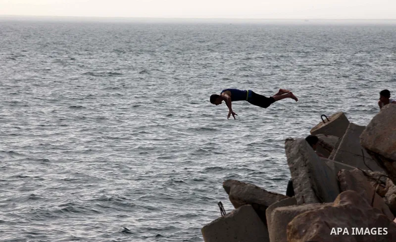 A Palestinian youth jumps into the Mediterranean Sea as he enjoys a warm day at the seaport in Gaza City on April 8, 2015. Photo by Ashraf Amra