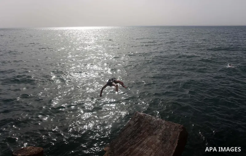 A Palestinian youth jumps into the Mediterranean Sea as he enjoys a warm day at the seaport in Gaza City on April 8, 2015. Photo by Ashraf Amra