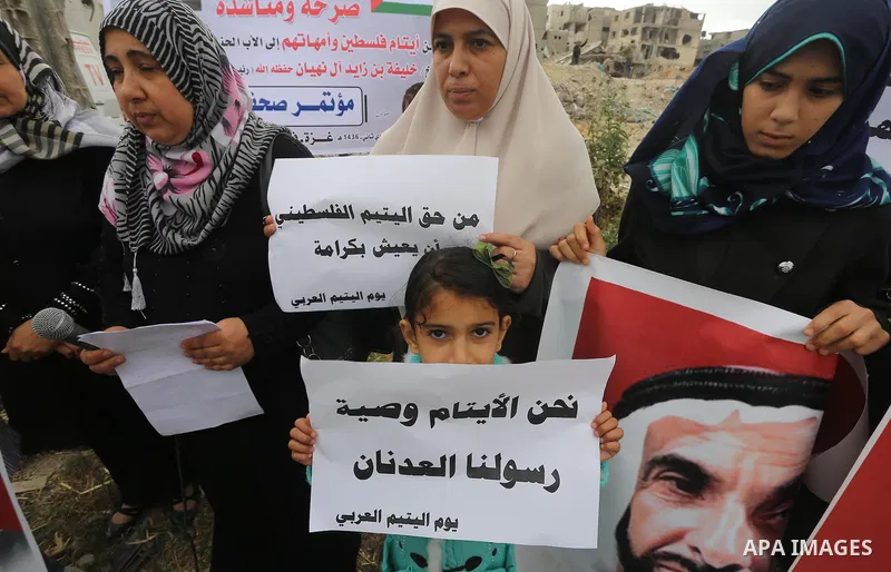 Relatives of Palestinian orphans hold banners during a protest against stop the payment of orphans aid in front of the rubbles of houses were destroyed during a seven-week Israeli offensive, in the east of Gaza City, on...