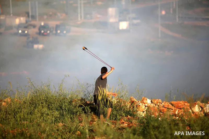 A Palestinian protester uses a sling shot to hurl stones towards Israeli security forces during clashes at a protest near the debris of a house that was demolished by Israeli army early today, in the West Bank village of...