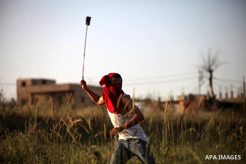 A Palestinian protester uses a sling shot to hurl stones towards Israeli security forces during clashes at a protest near the debris of a house that was demolished by Israeli army early today, in the West Bank village of...