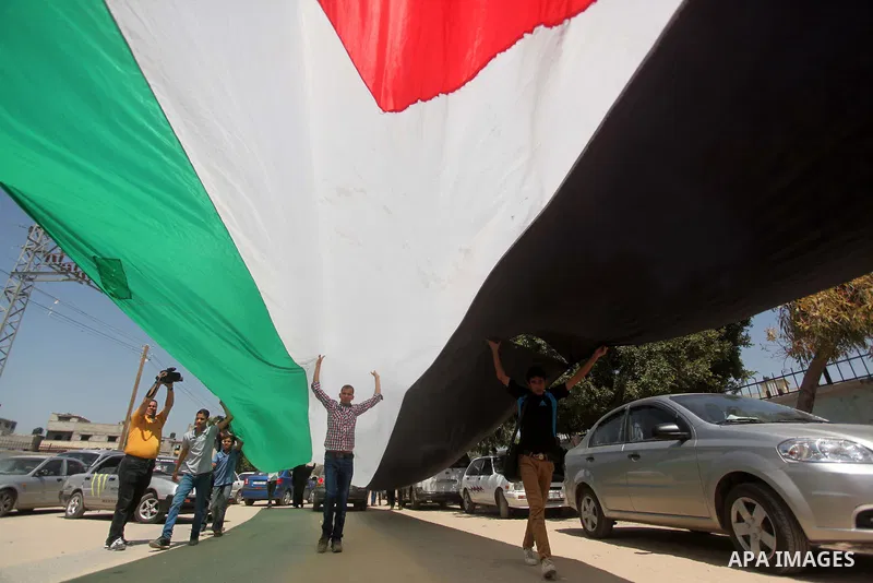 Palestinian youths hold a large Palestinian flag during a protest calling for an end in the political division and opening the Rafah crossing border, in Gaza city, on April 29, 2015. Photo by Ashraf Amra