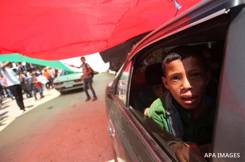 Palestinian youths hold a large Palestinian flag during a protest calling for an end in the political division and opening the Rafah crossing border, in Gaza city, on April 29, 2015. Photo by Ashraf Amra