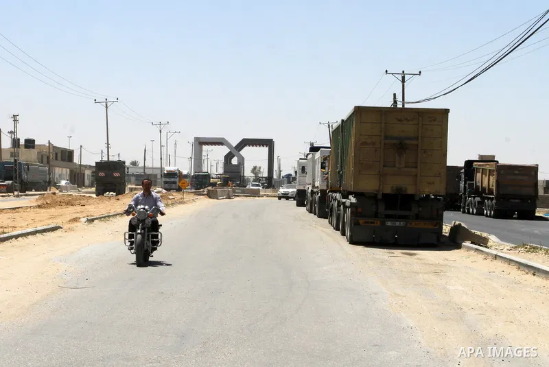 A Palestinian man rides a motorcycle past trucks as it waits outside the Kerem Shalom crossing in Rafah on April 29, 2015. Photo by Abed Rahim Khatib