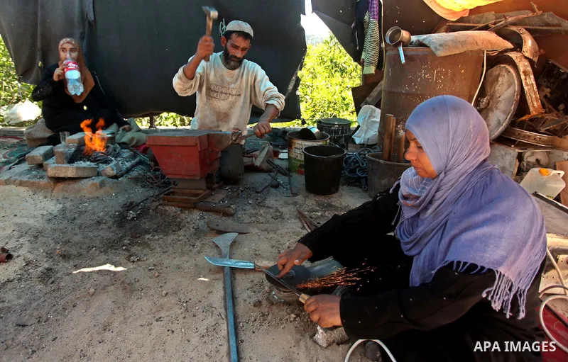 Aysha Ali, the wife of Ibraheem Mustafa, a 40-year-old Palestinian blacksmith, sharpens a handmade knife, as her husband hammers heated steel, at their small workshop in Gaza city on April 30, 2015. The ILO estimates tha...