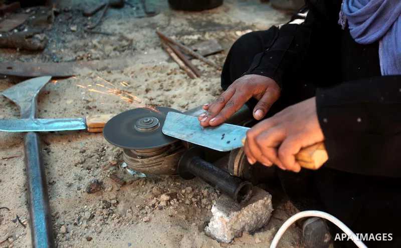 Aysha Ali, the wife of Ibraheem Mustafa, a 40-year-old Palestinian blacksmith, sharpens a handmade knife, at their small workshop in Gaza city on April 30, 2015. The ILO estimates that the 2014 conflict in Gaza raised un...