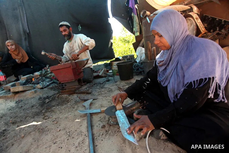 Aysha Ali, the wife of Ibraheem Mustafa, a 40-year-old Palestinian blacksmith, sharpens a handmade knife, as her husband hammers heated steel, at their small workshop in Gaza city on April 30, 2015. The ILO estimates tha...