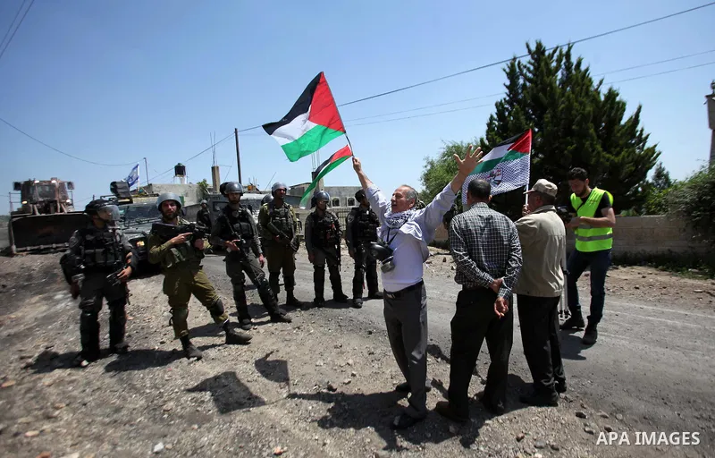 Palestinian protesters wave their national flags in front of Israeli security forces during a protest against the expropriation of Palestinian land by Israel in the West Bank village of Kafr Qaddum, near the northern cit...