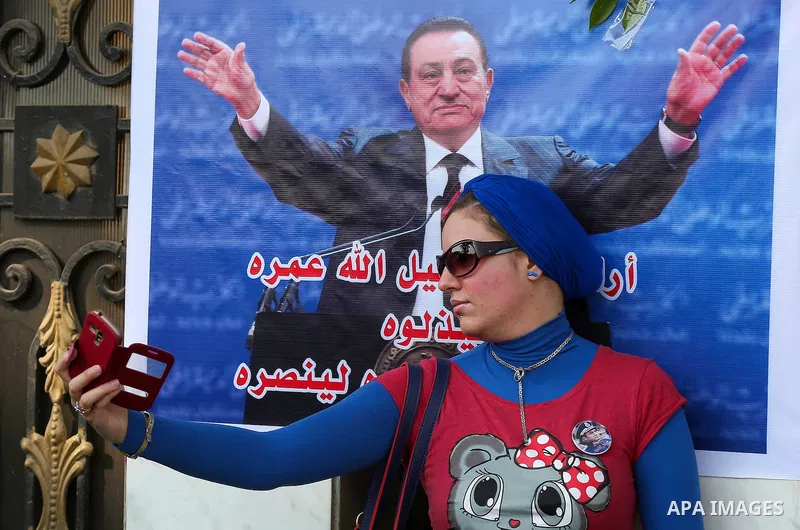An Egyptian supporter of former President Hosni Mubarak takes a selfie with his picture during a celebration to mark his 87th birthday, outside Maadi military hospital, near Cairo on May 4, 2015. An Egyptian legal author...