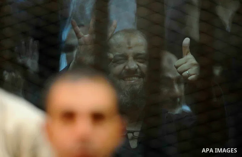 Egyptian Muslim Brotherhood top figure, Mohamed el-Beltagy flashes the four finger symbol known as "Rabaa" from behind the defendant's cage as the judge reads out the verdict sentencing him and more than 100 other defend...