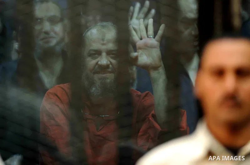 Egyptian Muslim Brotherhood top figure, Mohamed el-Beltagy flashes the four finger symbol known as "Rabaa" from behind the defendant's cage as the judge reads out the verdict sentencing him and more than 100 other defend...
