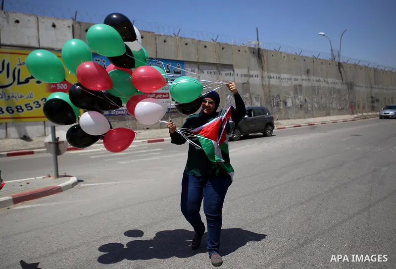A Palestinian woman holds flags and release balloons during a protest against the Israeli separation wall in the West Bank town of al-Ram, near Jerusalem, on May 21, 2015. Photo by Shadi Hatem