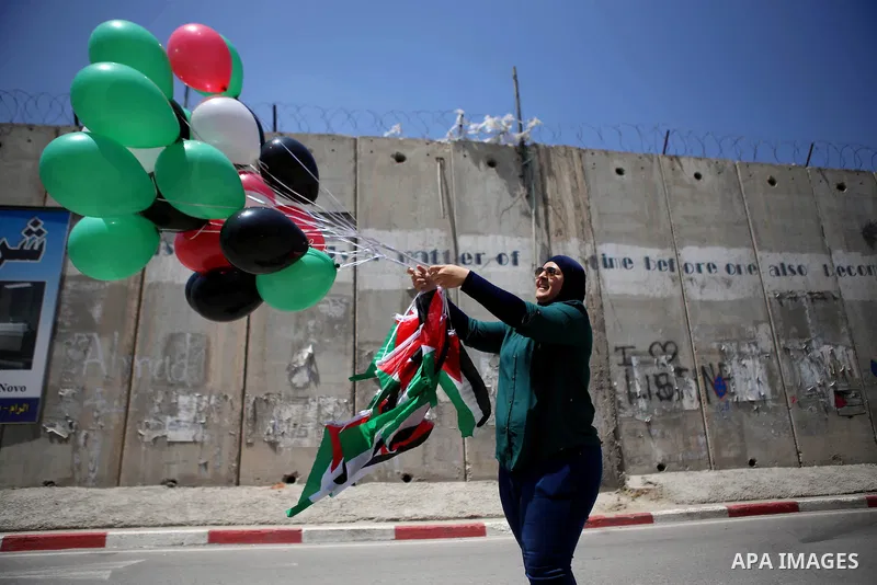 A Palestinian woman holds flags and release balloons during a protest against the Israeli separation wall in the West Bank town of al-Ram, near Jerusalem, on May 21, 2015. Photo by Shadi Hatem
