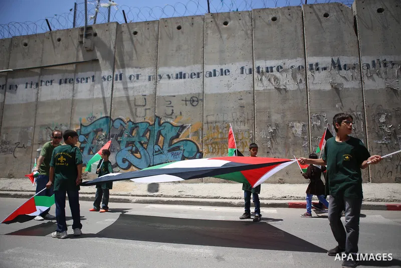 Palestinians hold flags during a protest against the Israeli separation wall in the West Bank town of al-Ram, near Jerusalem, on May 21, 2015. Photo by Shadi Hatem