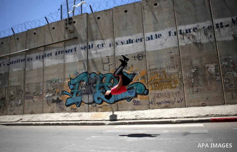 A Palestinian youth demonstrates his parkour skills during a protest against the Israeli separation wall in the West Bank town of al-Ram, near Jerusalem, on May 21, 2015. Photo by Shadi Hatem