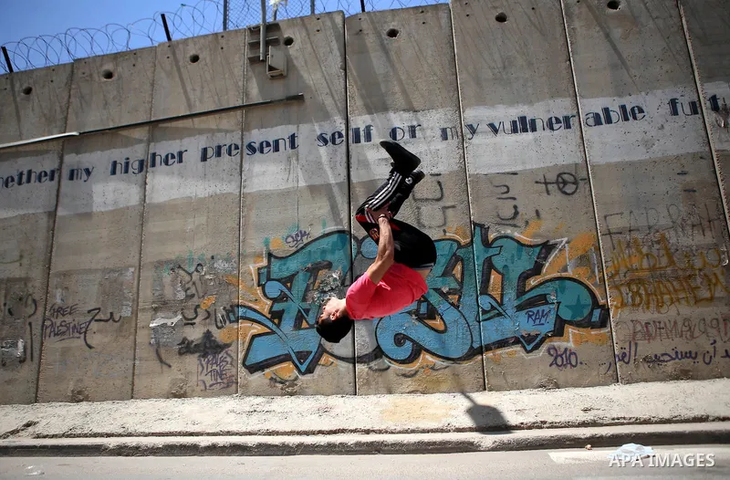 A Palestinian youth demonstrates his parkour skills during a protest against the Israeli separation wall in the West Bank town of al-Ram, near Jerusalem, on May 21, 2015. Photo by Shadi Hatem