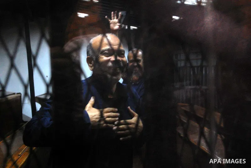 Egyptian Muslim Brotherhood top figures, Saad el-Katatni and Mohamed el-Beltagy flash the four finger symbol known as "Rabaa" from behind the defendant's cage during his trial for insulting the judiciary alongside 25 oth...