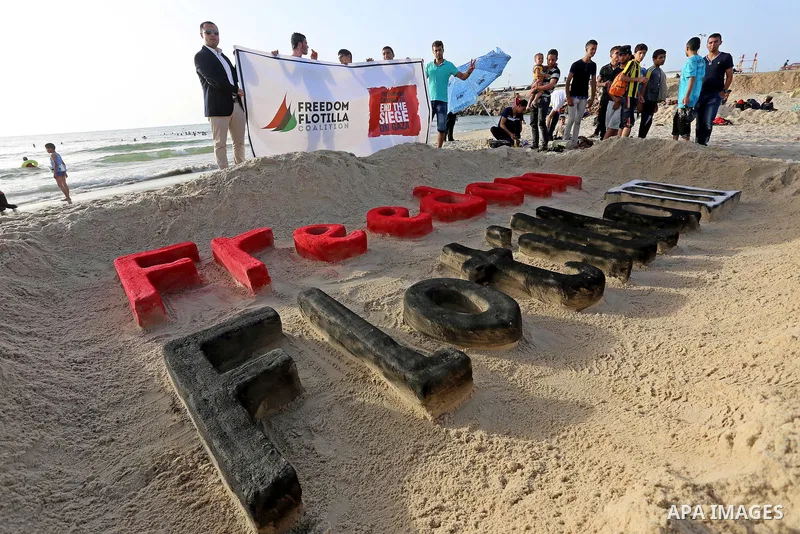 Palestinians hold a banner and stand in front of a sand sculpture reads ''Freedom Flotilla III'' at the beach of Gaza city, 24 May, 2015. The first ship taking part in Freedom Flotilla III last week set sail from Gothenb...