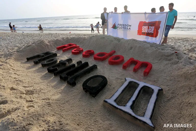 Palestinians hold a banner and stand in front of a sand sculpture reads ''Freedom Flotilla III'' at the beach of Gaza city, 24 May, 2015. The first ship taking part in Freedom Flotilla III last week set sail from Gothenb...