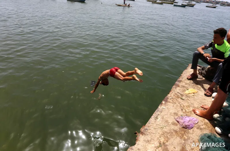 A Palestinian youth jumps into the Mediterranean Sea as he enjoys a warm day at the seaport in Gaza City on May 25, 2015. Photo by Mohammed Asad