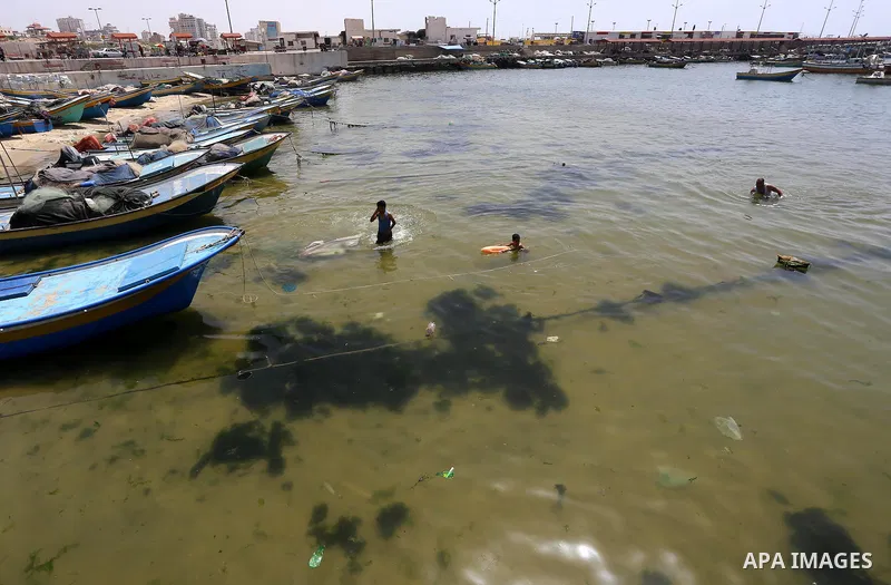 Palestinian youths swim into the Mediterranean Sea as they enjoy a warm day at the seaport in Gaza City on May 25, 2015. Photo by Mohammed Asad